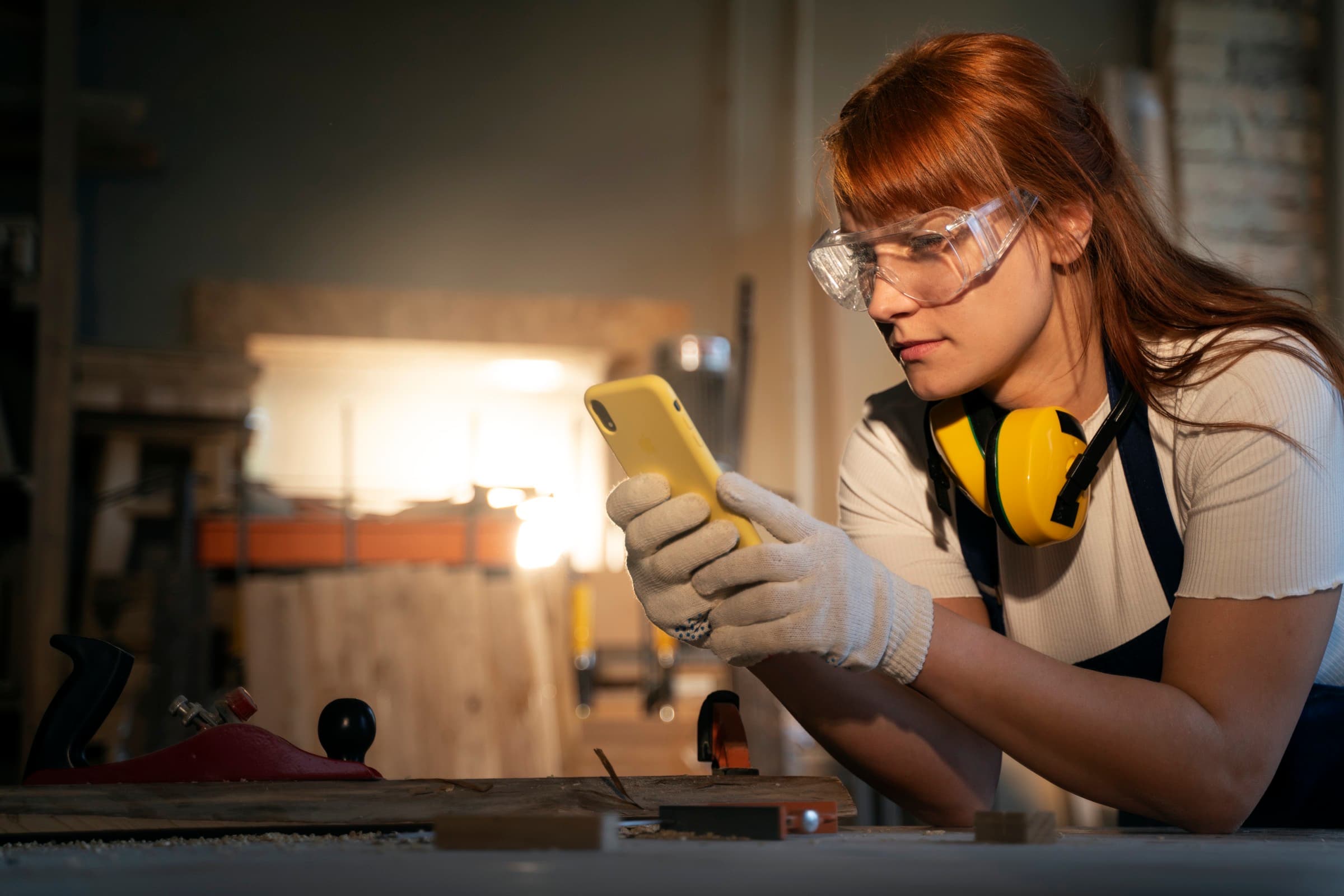 Artisane gantée, au travail, consultant une demande de chantier sur son téléphone.